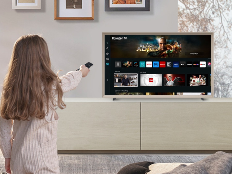 A girl is pointing the remote towards The Frame, which shows the Smart Hub home screen.